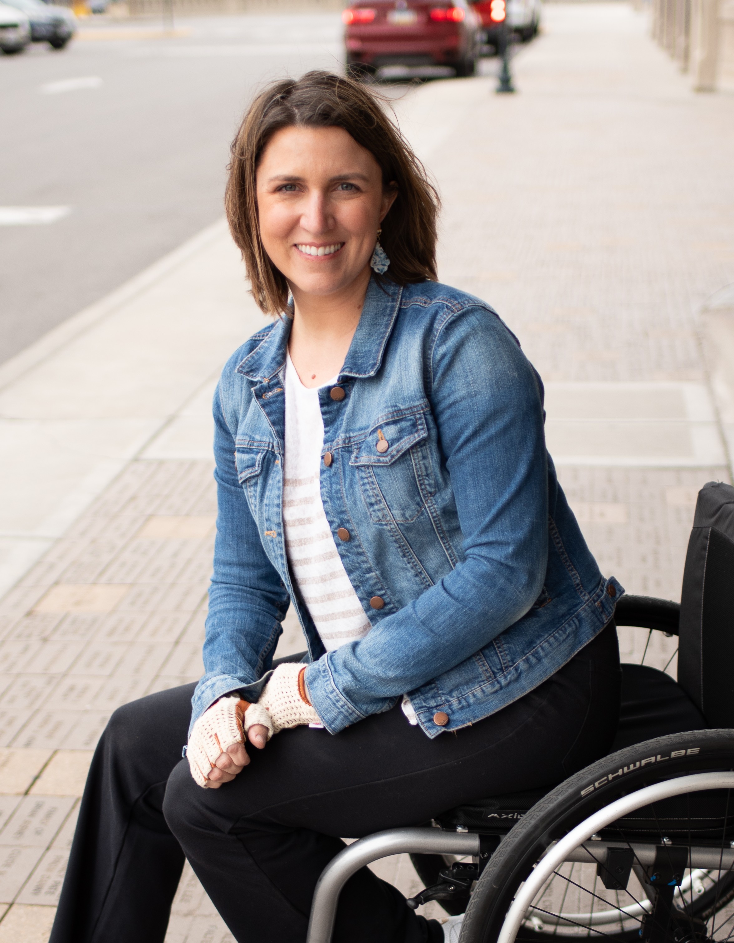 Stephanie smiles as she sits in a wheelchair, wearing a jean jacket